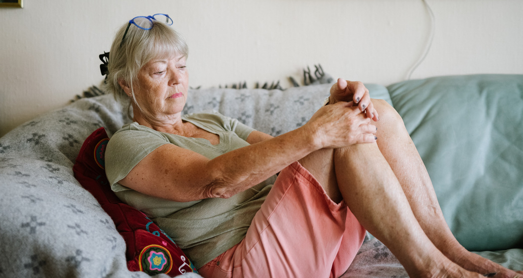 Äldre kvinna sitter med knäna uppdragna i soffan