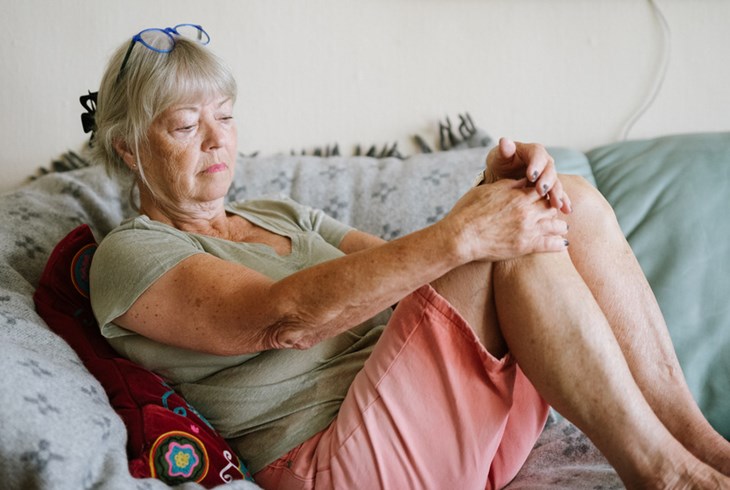 Äldre kvinna sitter med knäna uppdragna i soffan