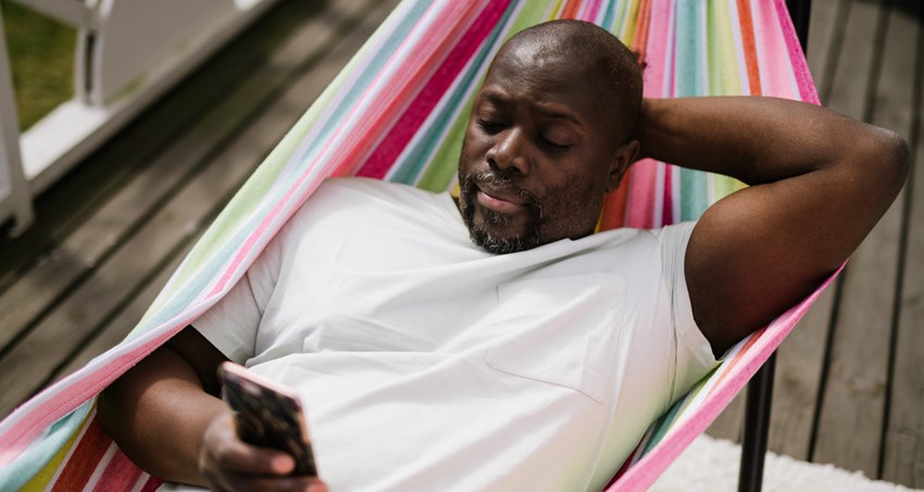 En man vilar i en hängmatta, han tittar på sin mobil.