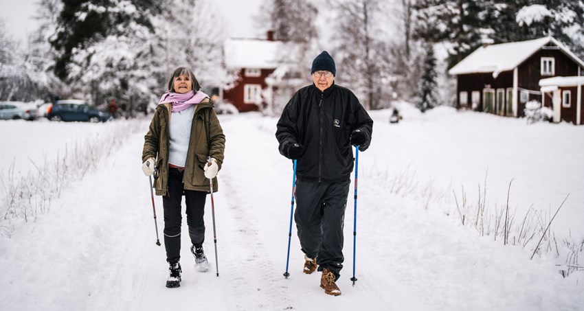 En man och kvinna går med stavar utomhus på vintern, det är snö.