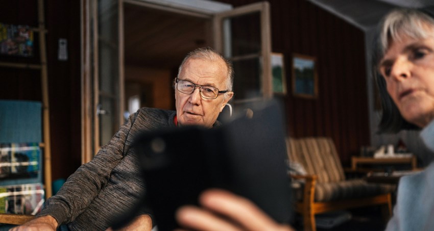 En man och en kvinna sitter utomhus och tittar på en mobil