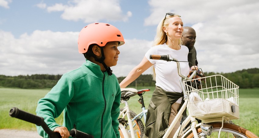 Två vuxna och ett barn står med varsin cykel i ett öppet och soligt landskap,
