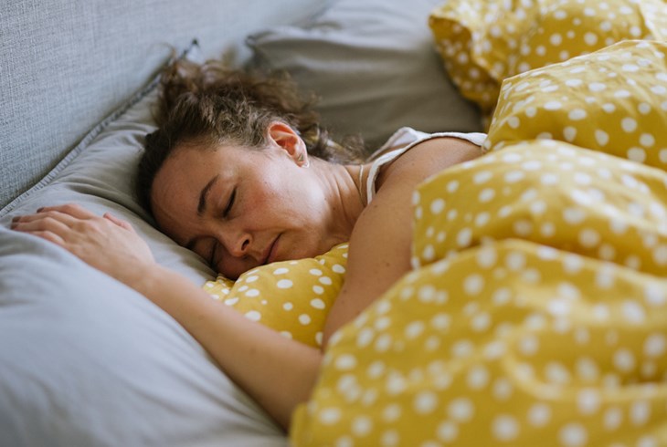 En kvinna ligger i sängen under täcket och sover.