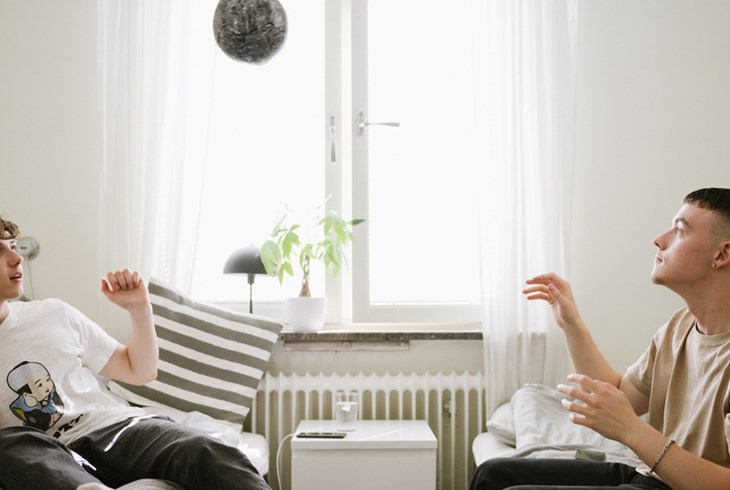 Två unga män sitter i varsin säng och kastar en boll mellan sig