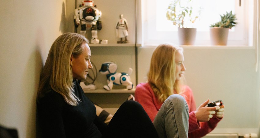 En kvinna och en flicka sitter i sen soffa i ett litet rum. De tittar på en skärm, flickan håller en handkontroll.