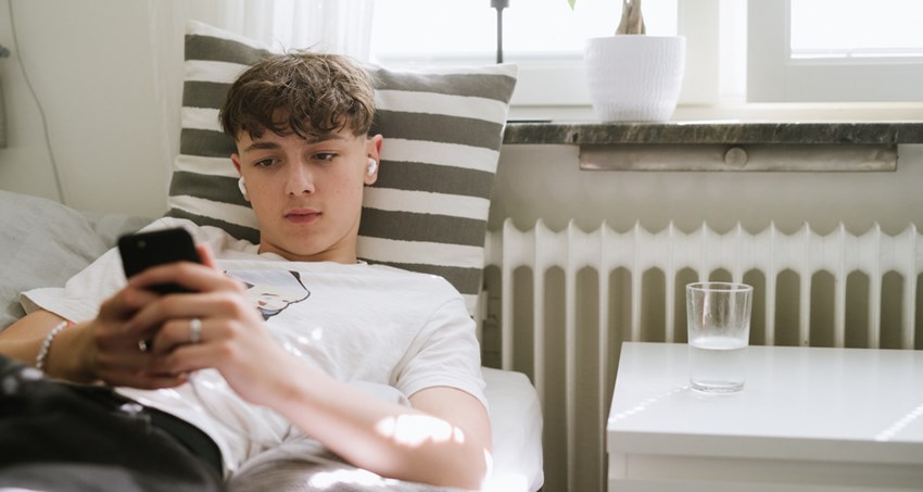Ung man ligger i en säng och tittar på sin mobil
