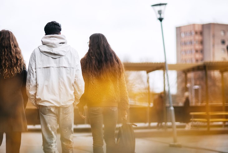 Tre ungdomar med ryggen mot kameran på ett förortstorg