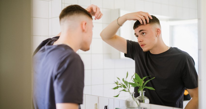 En ung kille står framför spegeln i badrummet. Han fixar frisyren.