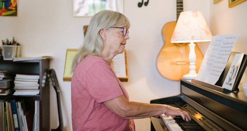 En äldre kvinna spelar orgel, i bakgrunden andra musikinstrument.